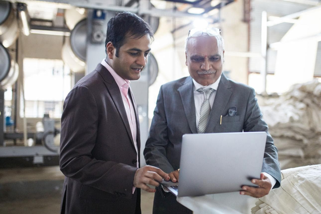 Two Indian business professionals reviewing a laptop in a manufacturing workshop