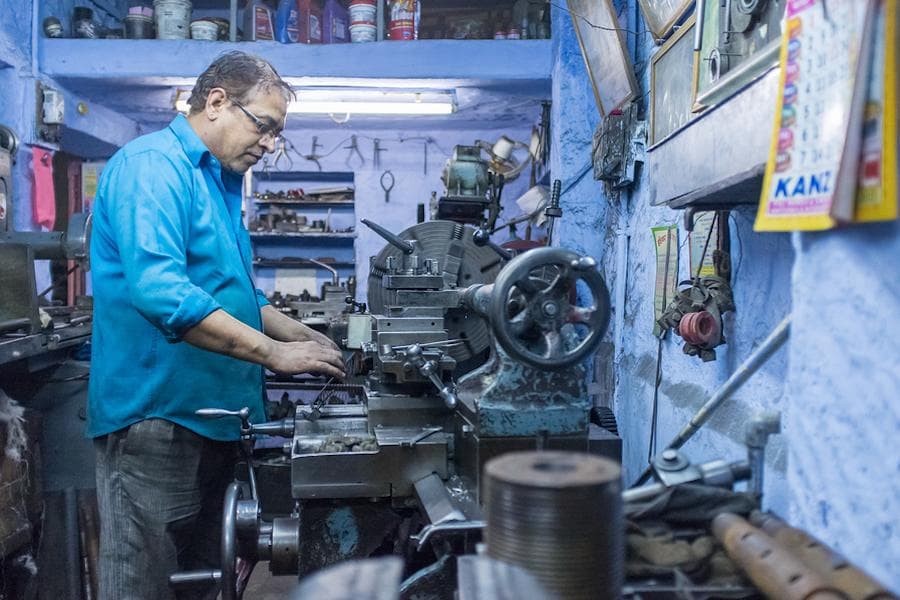 Indian micro-entrepreneur operating metalworking machinery in a small workshop