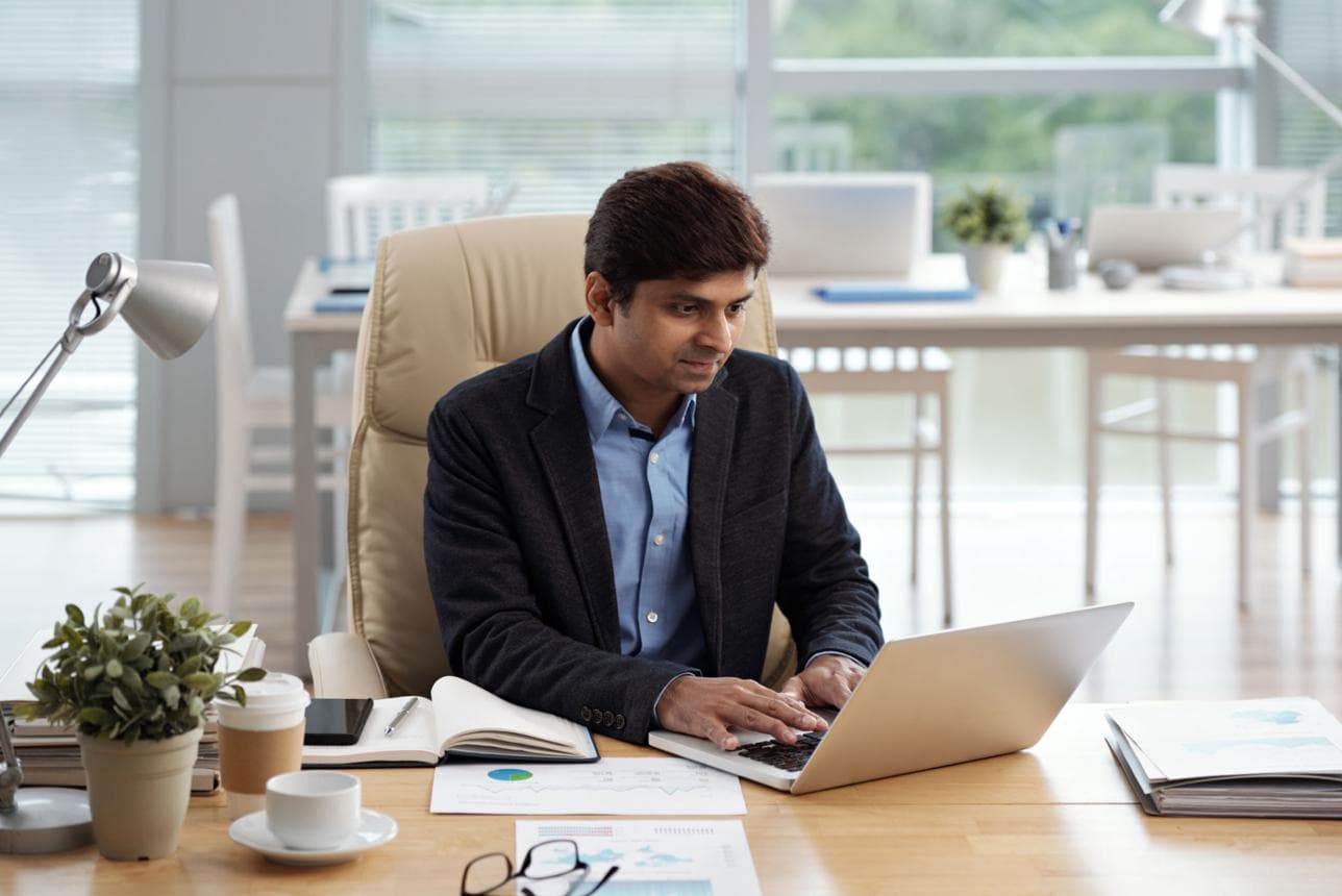 Indian small-business owner working on a laptop at an office desk